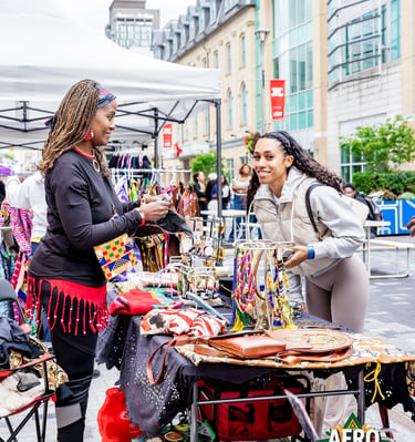 A customer shops for handmade African jewelry and accessories at an outdoor Afro Fiesta Festival market stall.