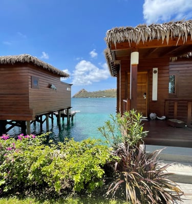 Luxury overwater wooden bungalows with thatched roofs overlooking tropical turquoise ocean water.