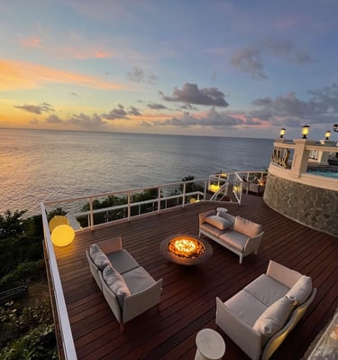 Luxury oceanfront terrace at sunset featuring a modern fire pit, cozy outdoor sofas, and a scenic sea view.
