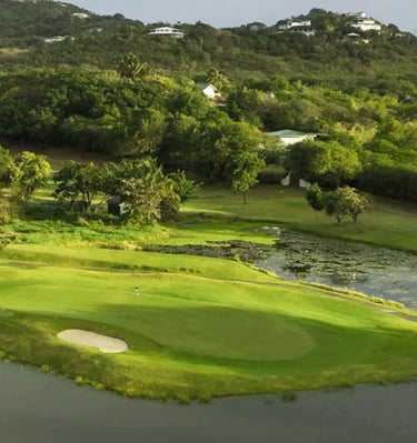A scenic tropical golf course green featuring a sand bunker and water hazards surrounded by lush hills.