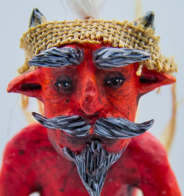 Red devil paper mask with horns, grey mustache, and a burlap headband.