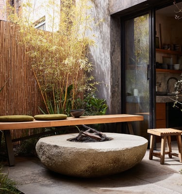 Modern outdoor patio featuring a stone fire pit, wooden bench, and bamboo privacy screen.
