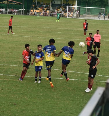 A group of teenage boys playing a competitive soccer match on a green field at a stadium.