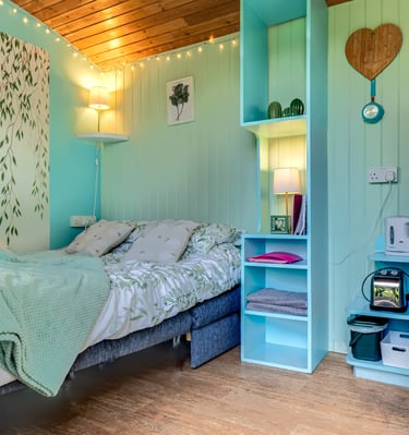 Cozy mint green garden room interior with a double bed, wood paneled ceiling, and turquoise shelving.