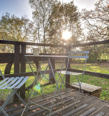 Metal bistro set on a wooden garden deck with golden hour sunlight filtering through autumn trees.