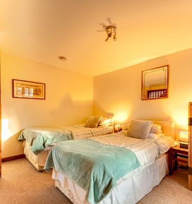 Cozy rustic bedroom with two twin beds, teal blankets, and wooden furniture under warm lighting.