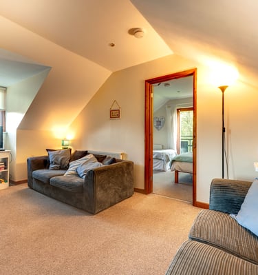 Cozy attic living room with grey corduroy sofas, television, and doorway leading to a bright bedroom.