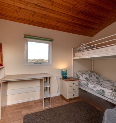 Small bedroom featuring a white bunk bed, wooden ceiling, and a desk under a window.