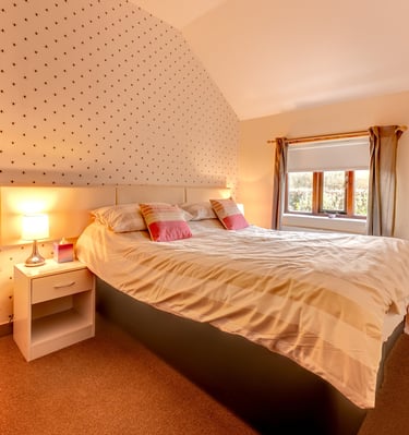 Cozy modern bedroom with patterned wallpaper, bedside lamp, and natural light from a window.