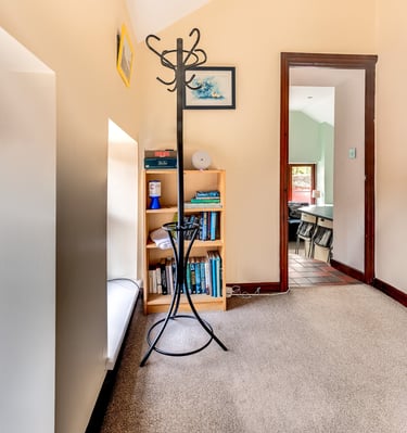 A carpeted hallway featuring a black metal coat rack and a wooden bookshelf with books.