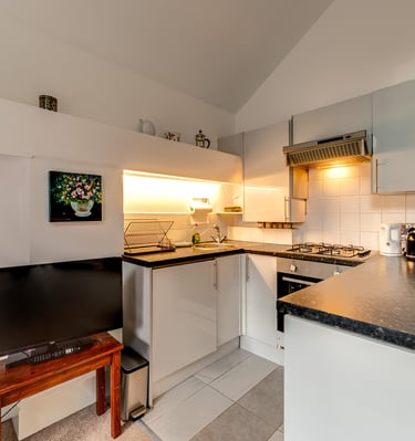 Modern small apartment kitchen with white cabinets, dark countertops, and integrated appliances.