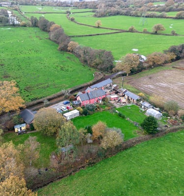 Aerial view of a rural farmhouse and green pastures in the English countryside during autumn.