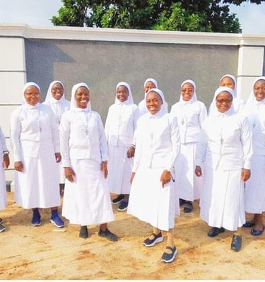 A group of smiling Catholic nuns in white habits posing together outdoors.