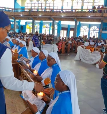 Catholic nuns in blue habits holding lit candles during a church ceremony with a congregation in the background.