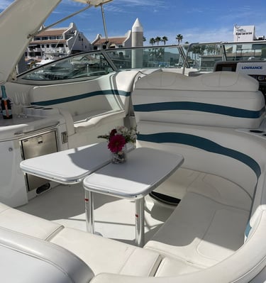 Luxury yacht deck with white leather seating, cockpit tables, and a champagne bottle near a sunny marina.