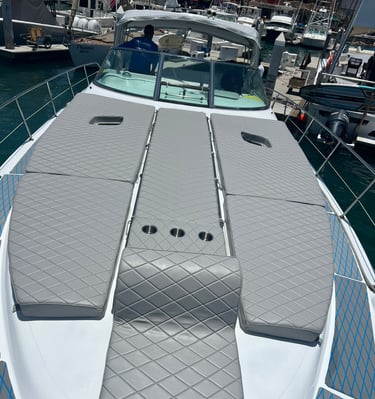 Luxury yacht deck featuring grey quilted sun pads and built-in cup holders docked at a sunny marina.