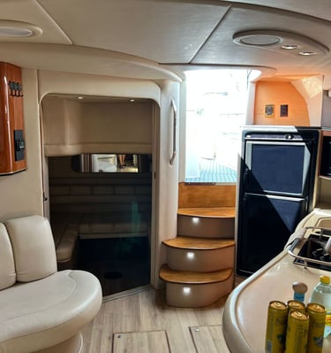 Luxury yacht cabin interior with leather seating, wooden cabinets, a compact galley kitchen, and stairs.