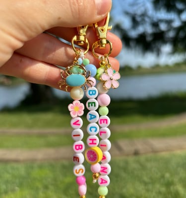 Mano sosteniendo dos llaveros, conformado por cuentas de letras, una flor y un cangrejo