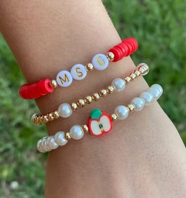 Mano con 3 pulseras diferentes, cuentas rojas, perlas, letras y un charm de manzana