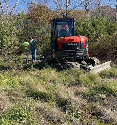 A Kubota mini excavator being used by JP Excavation for land clearing near a wooded area.
