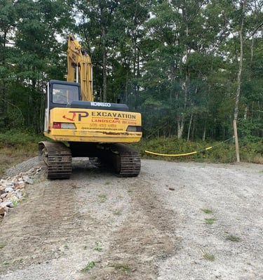 A yellow Kobelco excavator performing excavation and landscape design at a wooded construction site.
