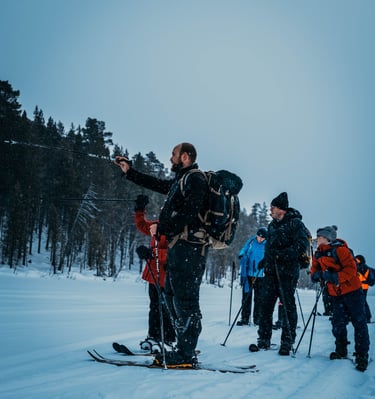 A group of hikers on a guided winter backcountry ski tour through a snowy forest landscape.