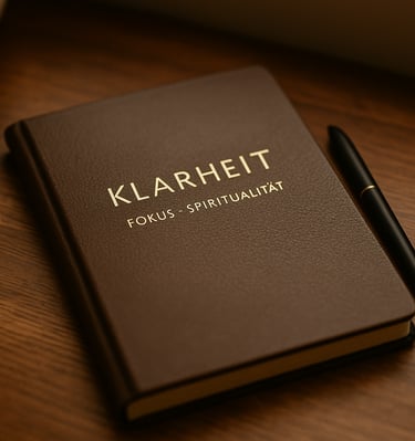 Dunkelbraunes Notizbuch mit der Aufschrift „Klarheit – Fokus – Spiritualität“ und Stift auf Holztisc