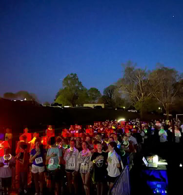 Racers lined up at the start line of a glow run event saying the pledge of allegiance