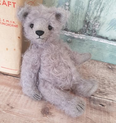 an adorable grey mohair handmade teddy bear leaning against a book