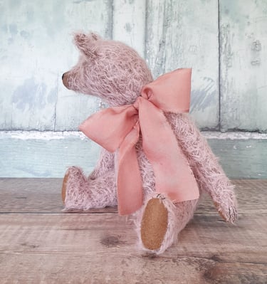 a pale pink teddy bear wearing a big pink bow