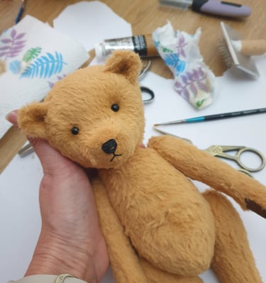 a teddy bear held in hands with art supplies in the background