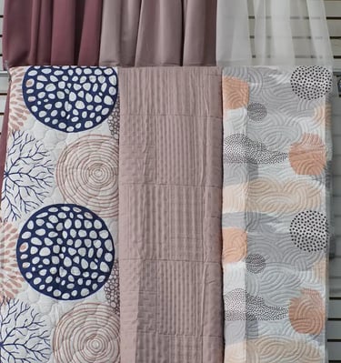 Muestras de colchas en frente de unas cortinas para enseñar los productos que se ofrecen.