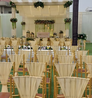 "Elegant outdoor wedding setup with gold chairs draped in white fabric, floral arrangements, string