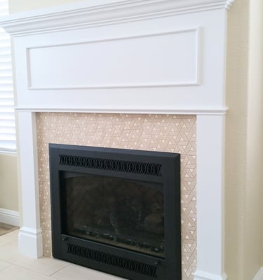 black fireplace with mixed media surround of triangular tan tile work surrounded by painted white wood work and mantle.