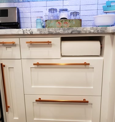 Custom white cabinetry with copper hardware and built in paper towel dispenser. Colorado Springs custom cabinets.