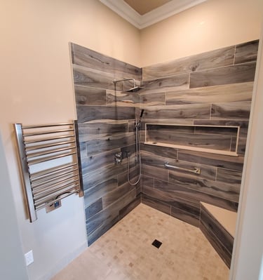 modern bathroom shower renovation with woodgrain tile, long cut in shelf, built in seat, and heated towel rack. El Paso CO.