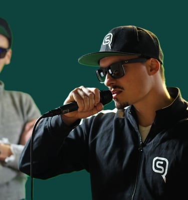 a man in a dark blue jacket with a black cap and sunglasses is holding a microphone