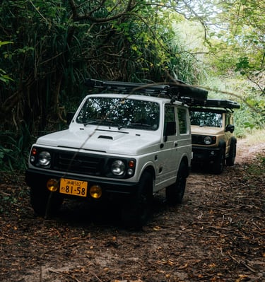 Two off-road Suzuki Jimny camping cars driving through a lush forest trail in Okinawa. | Evertrail Okinawa