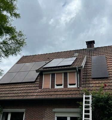 Black solar panels installed on a brown tile roof of a brick house under a cloudy sky.