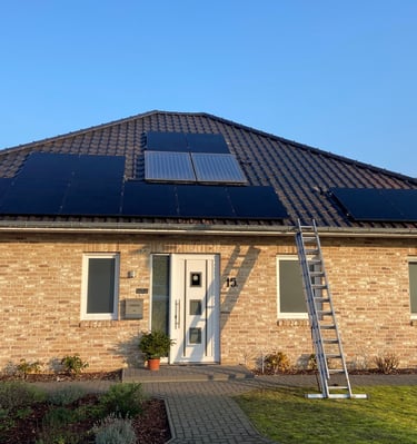Residential brick house with solar panels installed on a dark tiled roof and a ladder against the gutter.