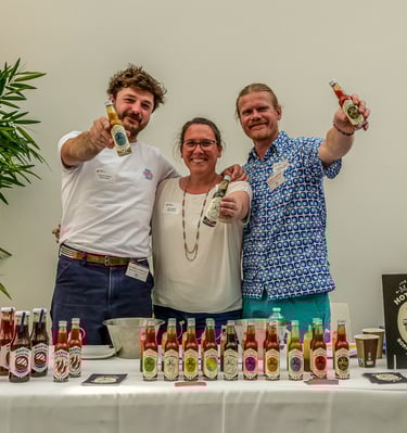 Deux hommes et une femmes qui tendent leurs bouteilles de sauces pimentées