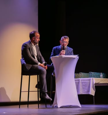 Deux personnes assises sur des tabourets sur scène qui discutent avec un micro