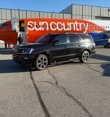 a black suv parked in front of a sun country air plane