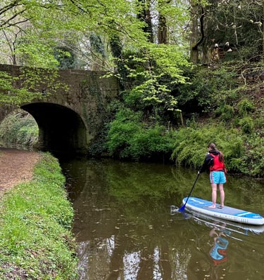 A paddle boarder paddles under a bridge on the Monmouthshire and Brecon canal on hire equipment from Bridge 76 Adventures