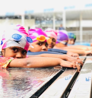 “Young swimmers in colorful caps resting on the pool edge during a lesson.”