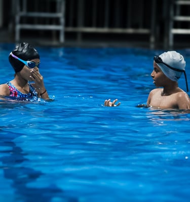 “Two children wearing swim caps and goggles practicing swimming in a pool.”