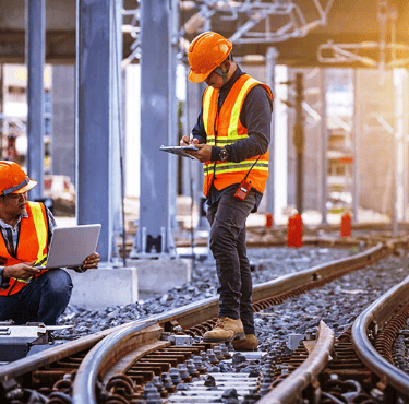 two men in safety vests standing on train tracks