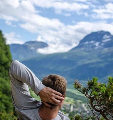 Homme allongé en montagne main gauche derrière la tête regardant un haut sommet un peu enneigé