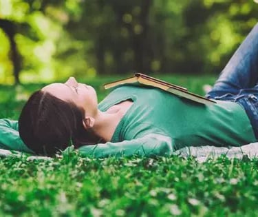 Femme allongée dans l'herbe, jambes repliées, pieds sur le sol et un livre ouvert sur sa poitrine