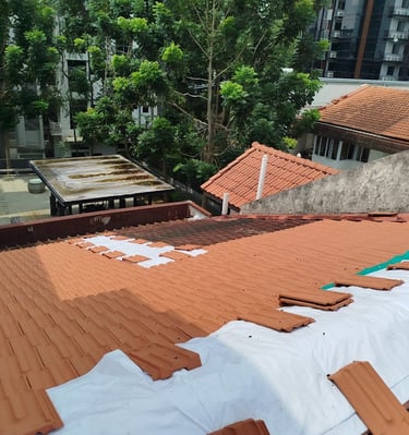 Roofer installing new terracotta roof tiles over a white waterproof membrane on a residential building.